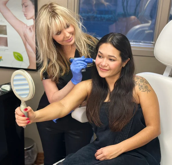 Tamra Bedford performing microneedling on a patient who is holding a mirror